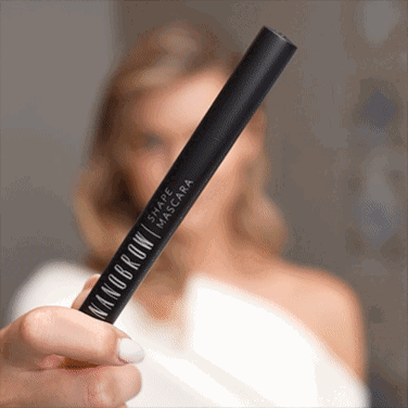 A blue-eyed woman in a white dress applying the Shape Mascara